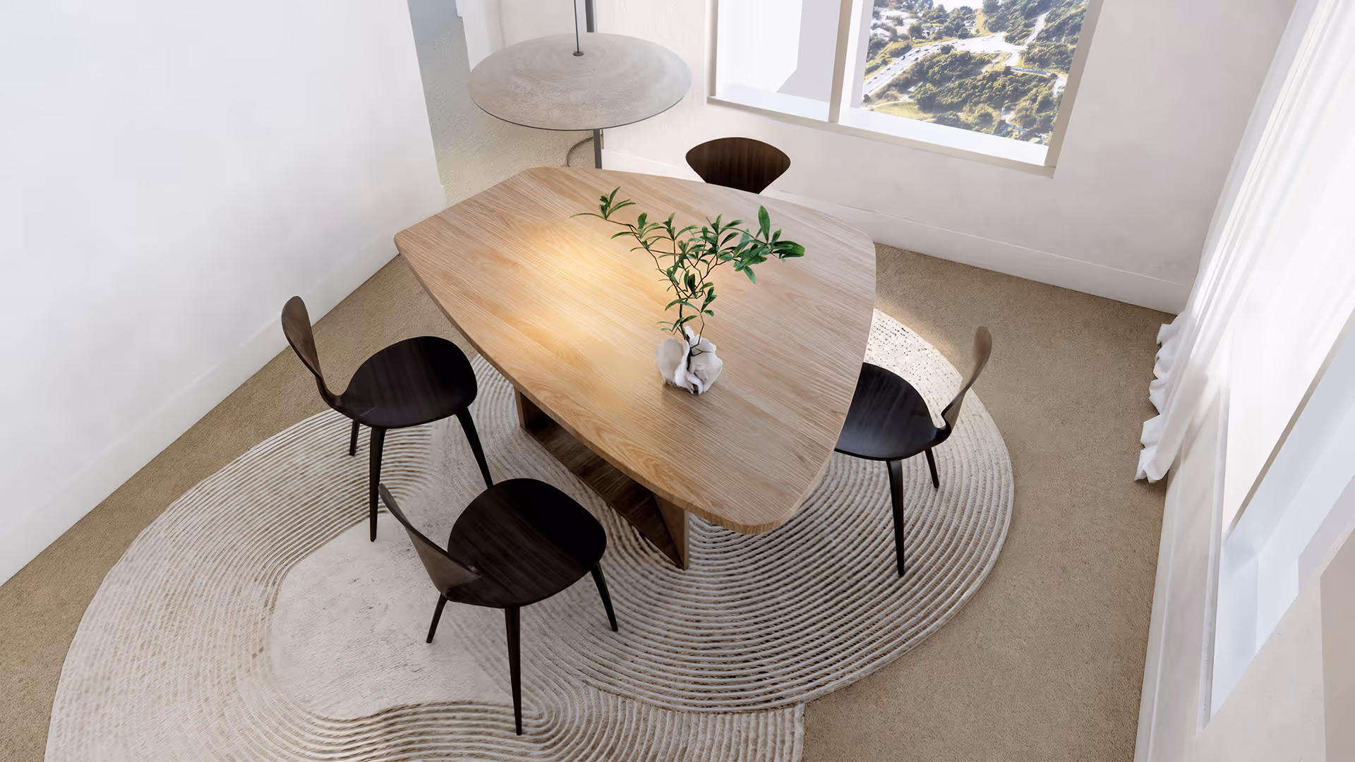 From above, the space reads like a geometric composition. The triangular table and circular rug play with form and flow, while the four chairs form a balanced cross-like layout. The pendant light appears as a floating disc, echoing the rug’s pattern and unifying the space through shape and light.