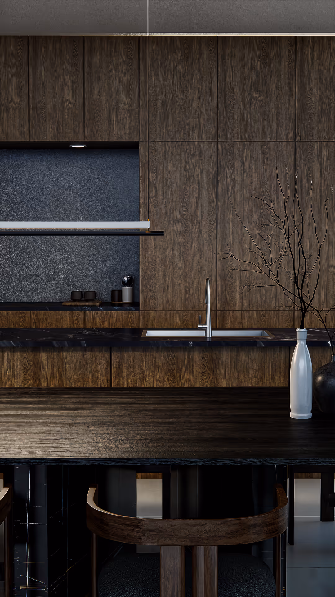 Wood grain and stone texture meet in quiet sophistication. The kitchen backdrop features deep walnut cabinetry paired with a matte stone backsplash, echoing the dining table’s raw tactility. A single ceramic branch completes the scene with sculptural restraint.