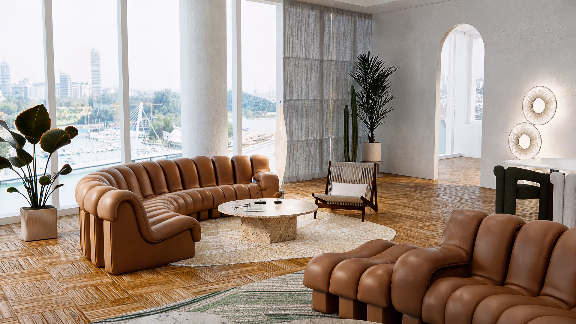 A curved modular sofa in brown leather anchors the room with a sculptural yet grounded presence. The use of organic shapes—both in the furniture and accessories—creates a relaxed, flowing composition. The low, circular coffee table in off-white stone and warm wood flooring adds visual softness and a tactile sense of serenity.